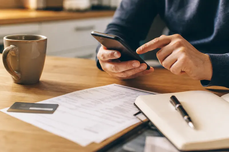 Main vérifiant un débit suspect sur smartphone près d’une carte bancaire.
