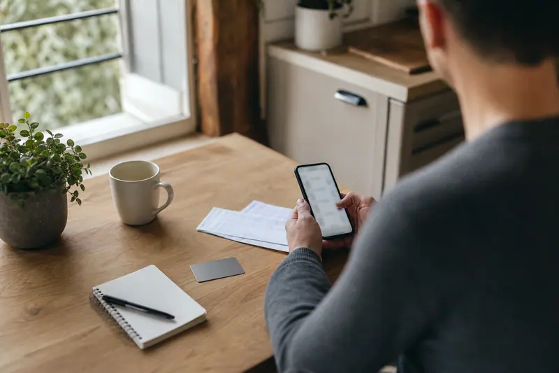 Client consulte son application bancaire près de documents de compte sur une table.