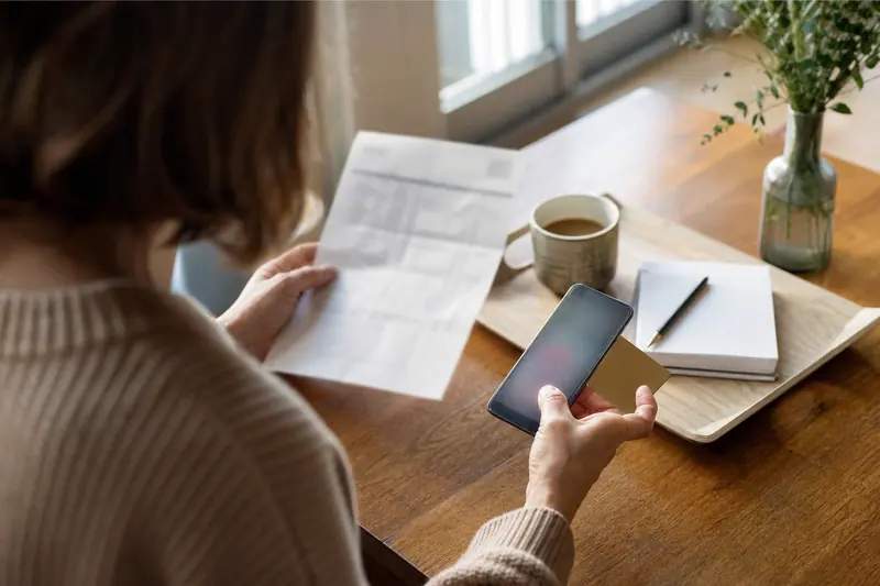 Client comparant documents bancaires, carte et smartphone sur une table lumineuse.
