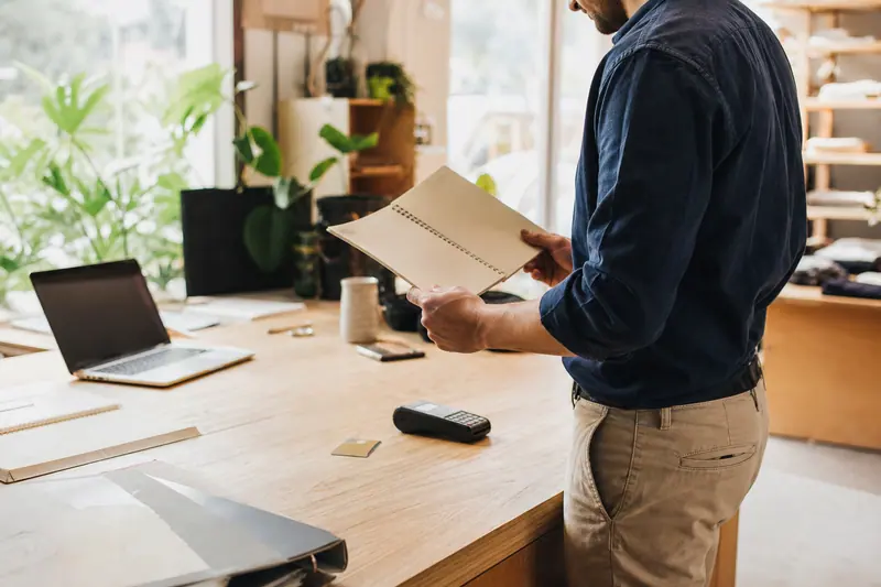 Entrepreneur organisant factures, carte et terminal de paiement sur son bureau.