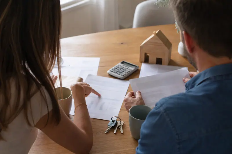 Couple comparant des documents de prêt avec clés et calculatrice sur une table.