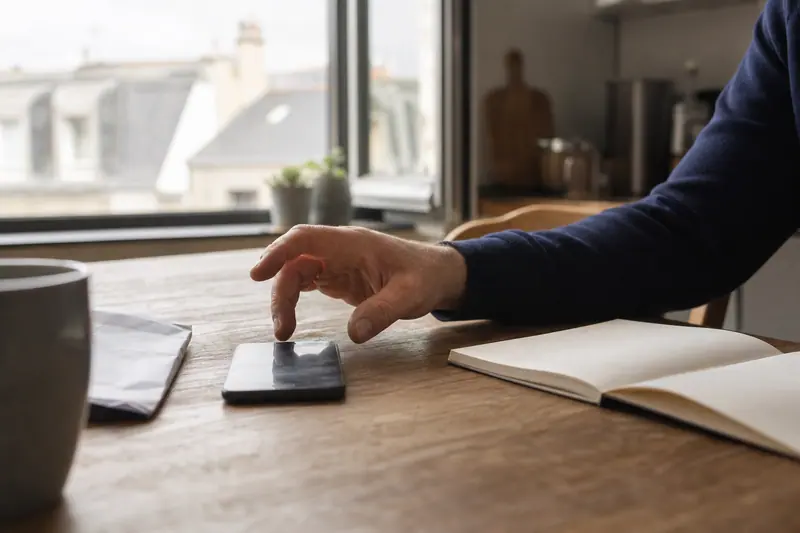 Main vérifiant prudemment un jeu-concours sur smartphone près de documents papier.