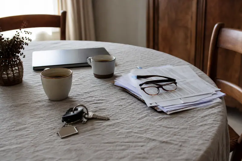 Clés de maison posées près de documents et de deux tasses de café sur une table en lin