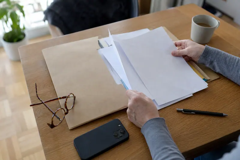 Mains triant des documents administratifs sur un bureau en bois à côté d'un smartphone