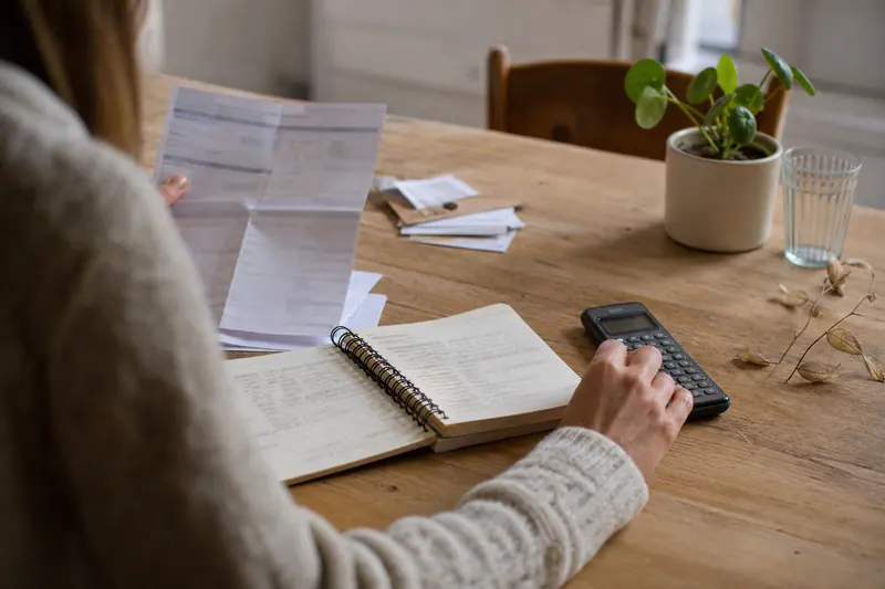 Mains comparant des documents d’épargne près d’une plante sur une table.