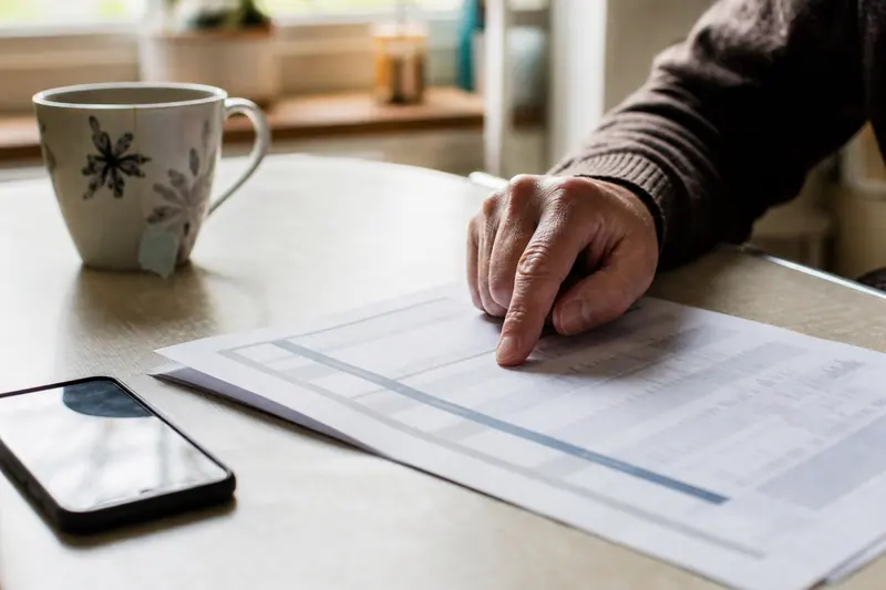 Main suivant du doigt une ligne sur un relevé bancaire posé sur une table de cuisine