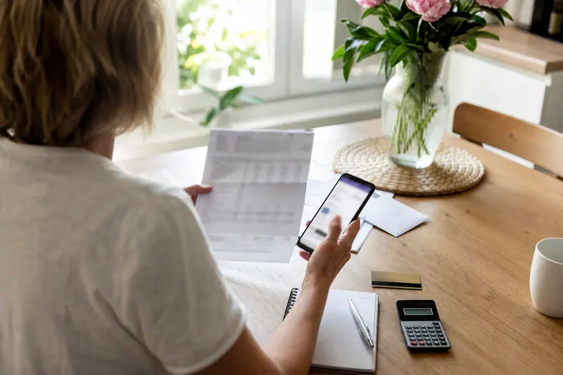 Comparaison de documents bancaires et d’un smartphone sur une table de cuisine.