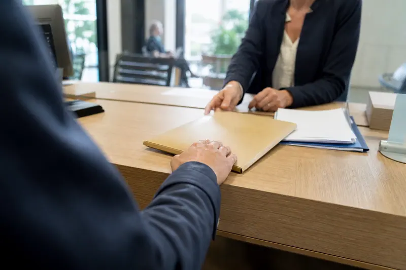 Main posant une enveloppe et un dossier de justificatifs sur le comptoir d'une agence bancaire
