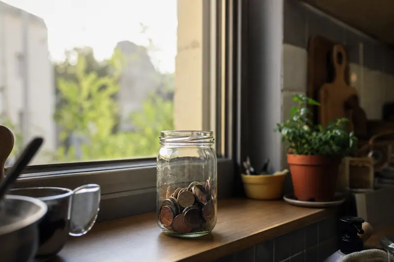 Bocal en verre avec des pièces de monnaie posé sur un rebord de fenêtre