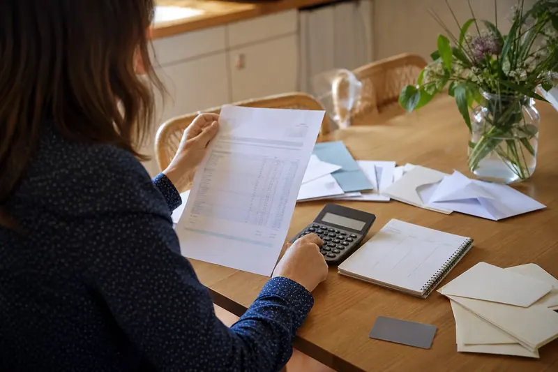 Documents financiers, calculatrice et carte bancaire posés sur une table de cuisine.