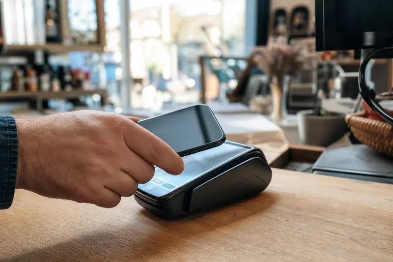Main tenant un smartphone Android près d’un terminal de paiement sans contact.