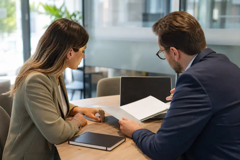Deux professionnels échangent sur un dossier dans une agence bancaire moderne.