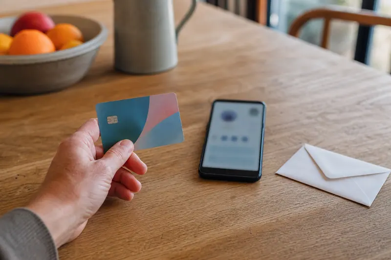 Main tenant une carte au visuel coloré près d’un smartphone sur une table.