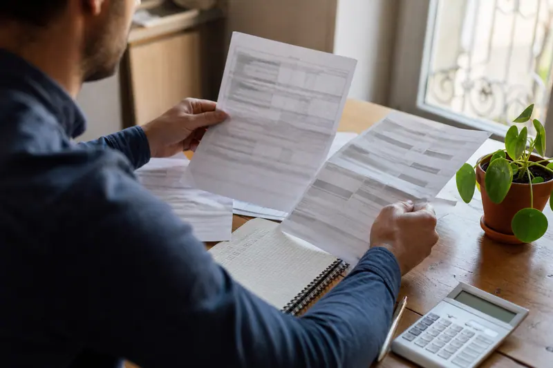Personne comparant des documents d’épargne responsable sur une table en bois.