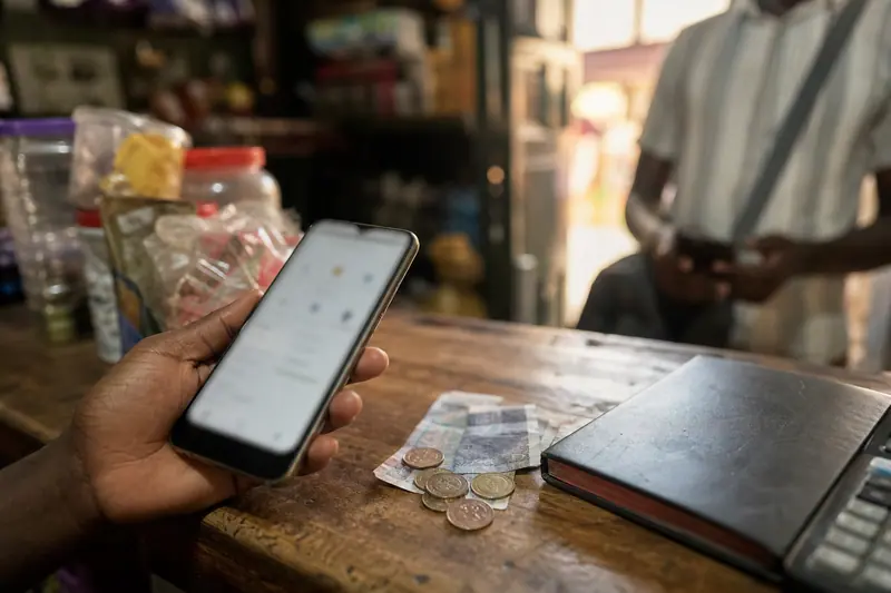 Paiement mobile chez un agent de proximité avec téléphone et espèces.