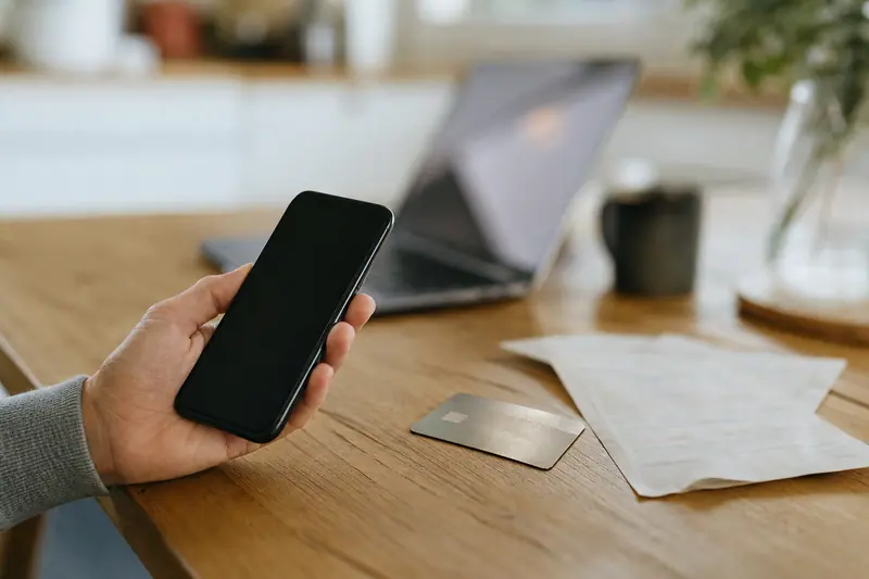 Personne vérifiant un ancien paiement avec smartphone et carte bancaire sur une table.