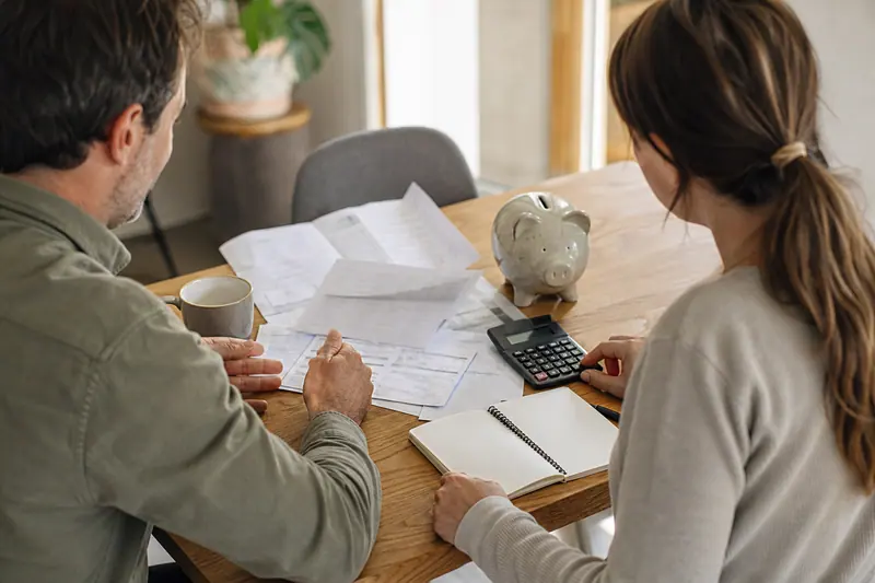 Couple examinant son budget domestique avec calculatrice et documents sur une table.