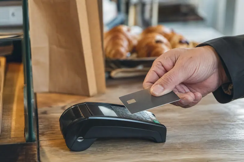 Main payant sans contact sur un terminal dans une boulangerie française.