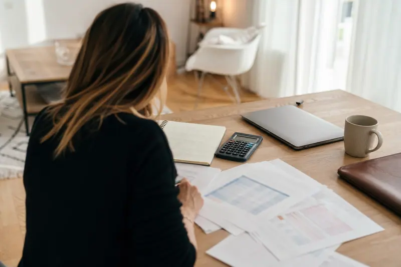 Personne analysant des documents chiffrés et une calculatrice sur une table claire.