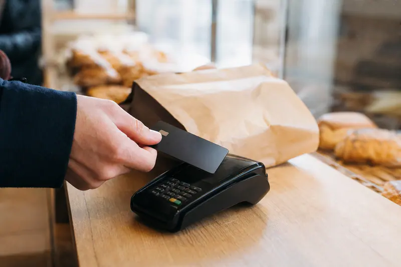 Main approchant une carte bancaire d’un terminal de paiement sans contact.