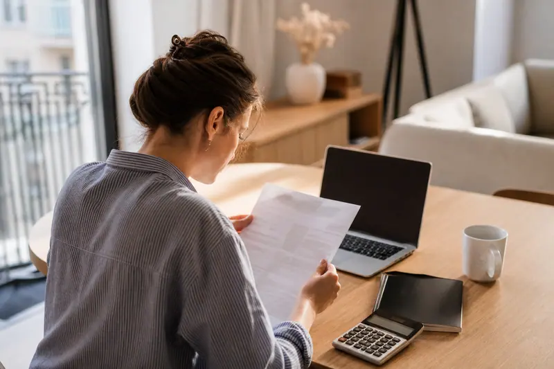 Salariée examinant ses documents de paie et une calculatrice à domicile.