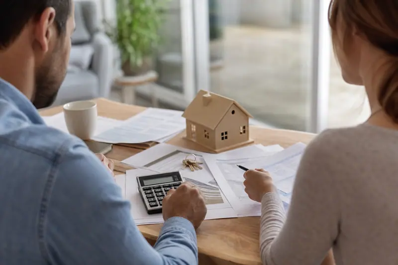 Couple examinant des documents de prêt immobilier avec calculatrice et clés sur une table.