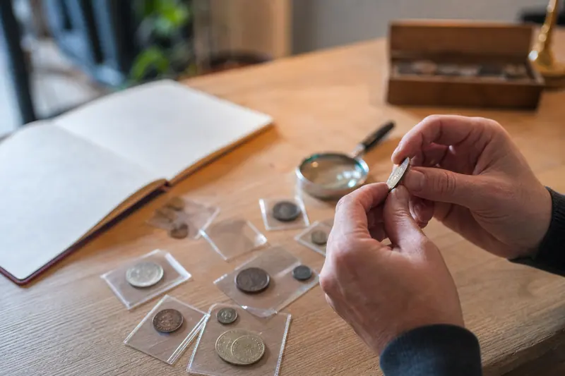 Pièces anciennes examinées avec une loupe sur une table en bois.