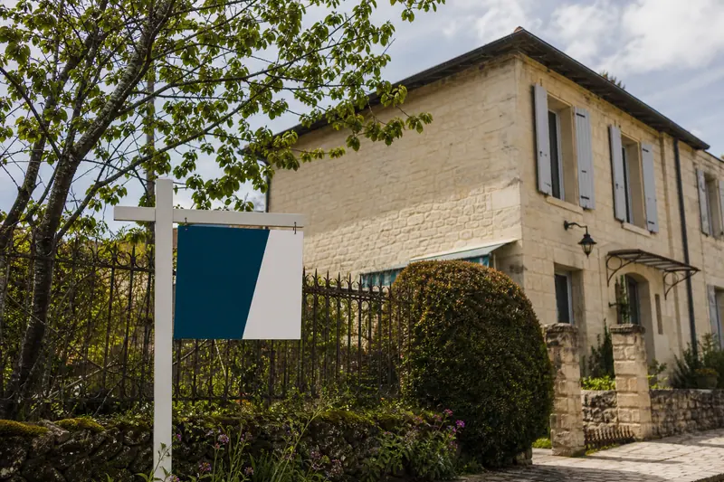 Panneau à vendre planté devant une maison en pierre