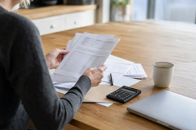 Personne examinant des relevés bancaires et calculant des frais contestés à domicile.