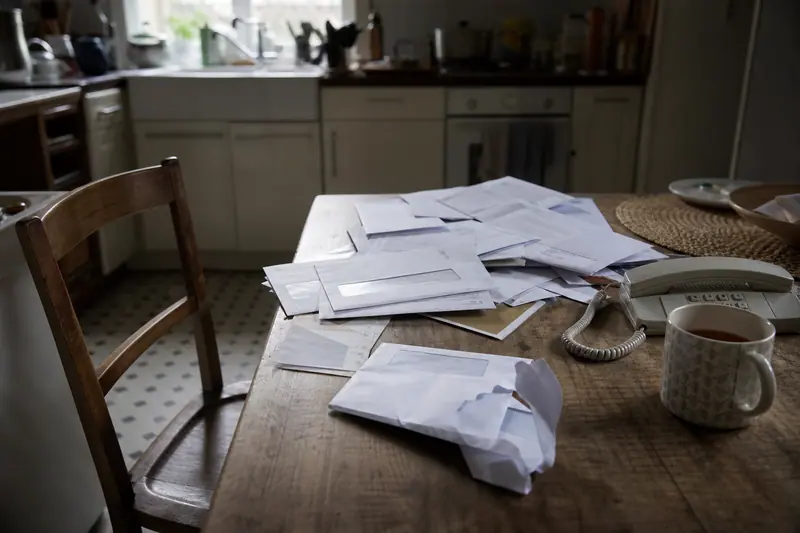 Courriers administratifs ouverts empilés sur une table de cuisine près d’une tasse de thé