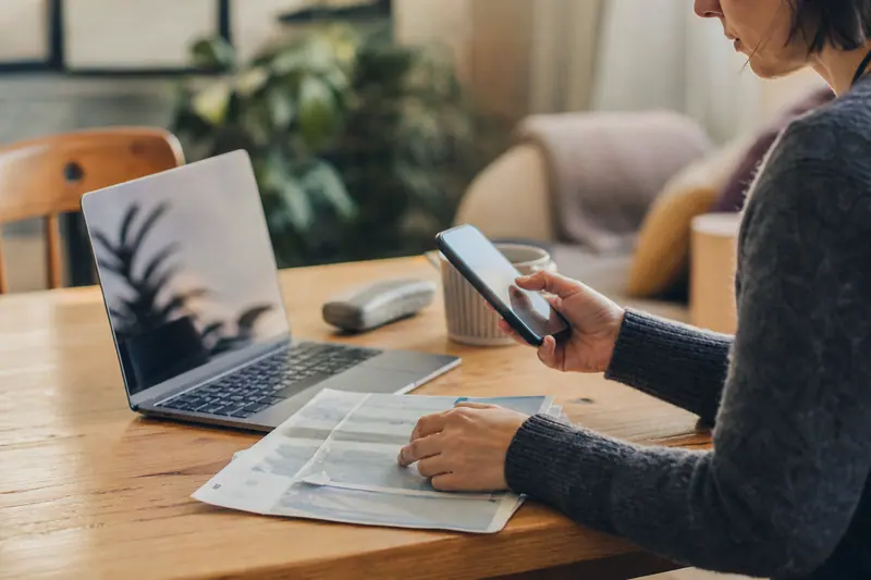 Personne consultant son téléphone près d'un ordinateur portable pour un virement